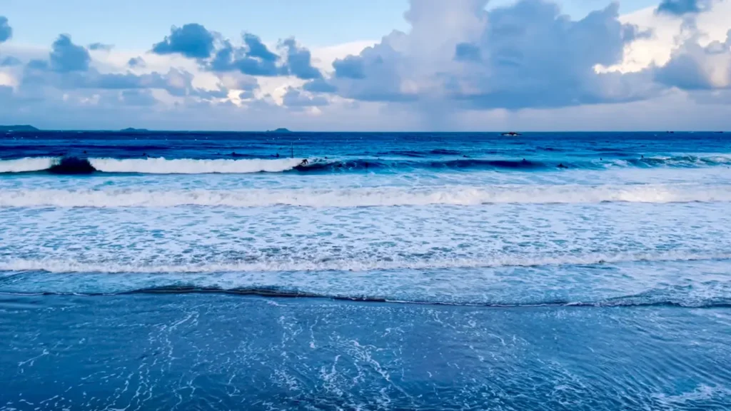 Surfeur chevauchant les vagues à la plage de Trestrignel Perros-Guirec avec l'océan Atlantique bleu profond et ciel nuageux dramatique