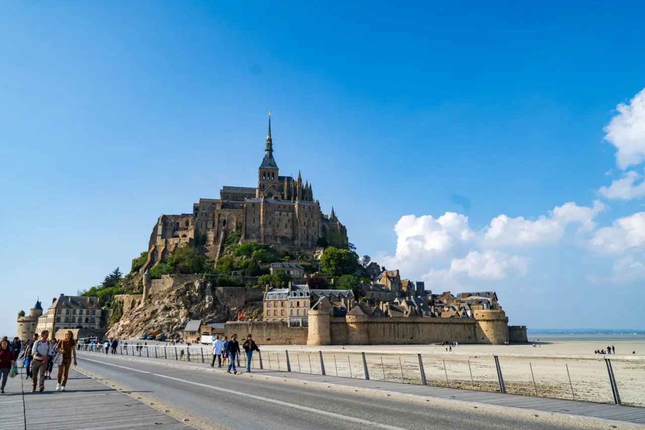 Vue de l'abbaye du Mont Saint-Michel depuis la sortie de la passerelle avec touristes s'éloignant