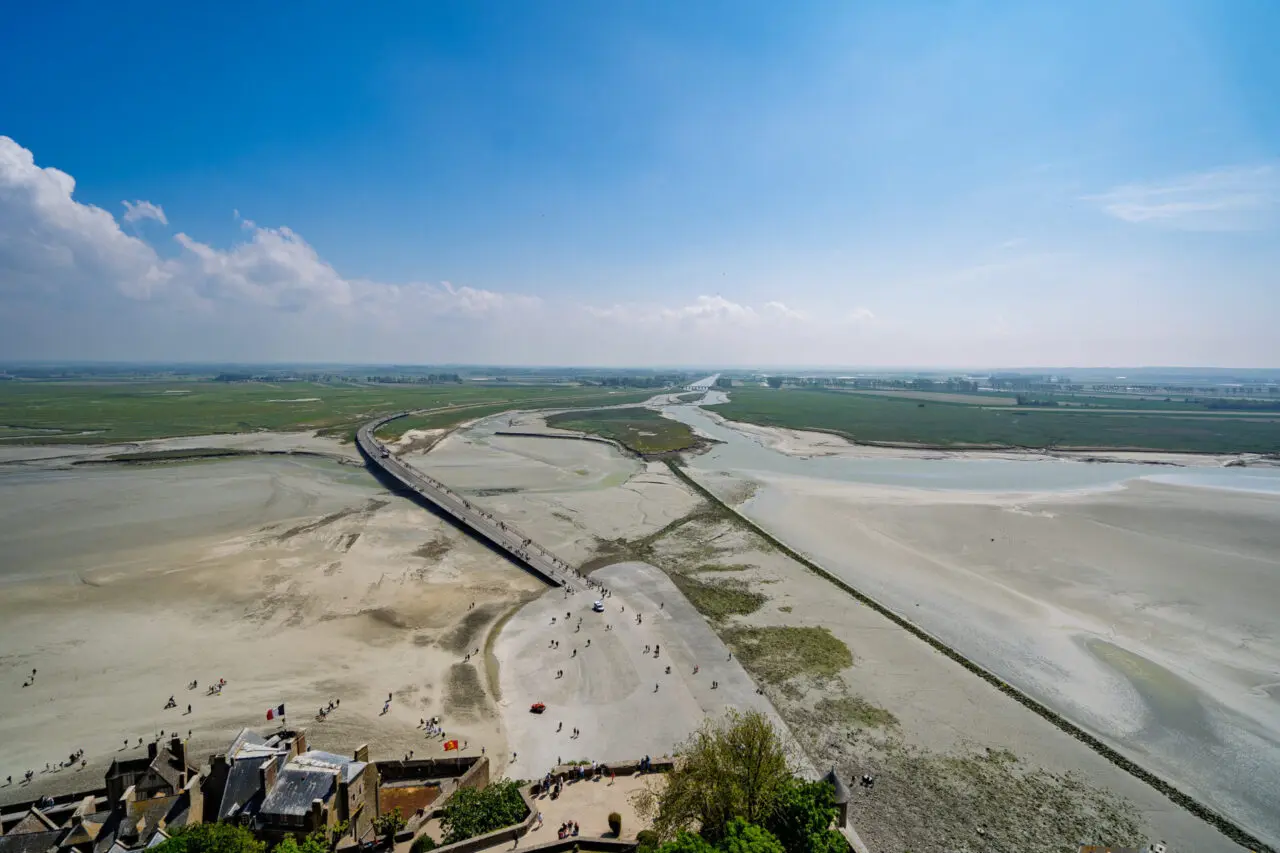 Vue aérienne depuis les remparts du Mont Saint-Michel montrant la passerelle, les grèves et les petites personnes en bas